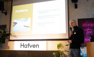 Ein Mann hält einen Vortrag bei Hafven. Auf der Leinwand eine Folie mit dem Titel „Probleme" auf Deutsch.