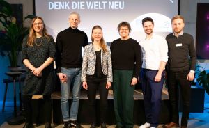 Sechs Personen stehen nebeneinander vor einer Leinwand mit der Aufschrift „Denk die Welt neu".