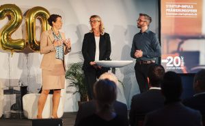 Drei Personen auf einer Bühne bei der Startup-Impuls Prämierungsfeier zum 20-jährigen Jubiläum.
