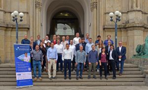 Gruppenfoto von ca. 30 Personen auf Treppe eines Gebäudes, daneben ein Banner mit Aufschrift „Wasserstoff".