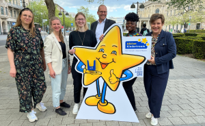 Sechs Personen posieren mit einem großen Pappaufsteller einer lächelnden Stern-Figur mit "Aktion Kindertraum"-Logo.