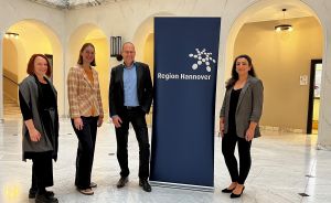 Vier Personen stehen in einem Foyer neben einem Banner mit der Aufschrift „Region Hannover".