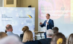 Mann präsentiert vor Publikum. Hinter ihm Banner „WirtschaftsDienst" und Folie „Herausforderungen der Wärmewende", Hannover 2023.