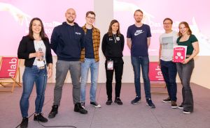 Sieben Personen stehen lächelnd auf einer Bühne vor einer rosa Leinwand mit der Aufschrift „leanlab".