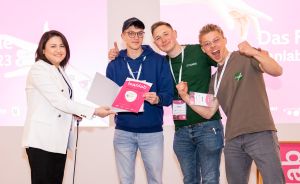 Vier Personen stehen auf einer Bühne; eine Frau überreicht einem jungen Mann ein Zertifikat mit „leanlab"-Logo.