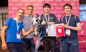 Vier Männer posieren vor einem Leanlab-Banner, einer hält eine Zebra-Figur, ein anderer ein Zertifikat.