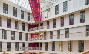 Mehrstöckiges Atrium mit Glasdach, bunten Wandfeldern in Pink/Lila und Holzgeländern auf mehreren Ebenen.