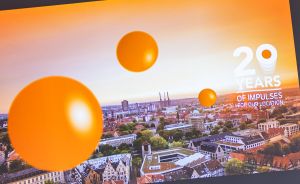 Luftaufnahme einer Stadt mit orangefarbenen Kugeln/Ballons und Text „20 Years of Impulses for our Location".