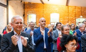 Gruppe von Menschen in Businesskleidung applaudiert in einem Veranstaltungsraum mit Backsteinwänden.