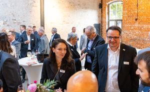 Personen in Business-Kleidung bei einer Networking-Veranstaltung in einem Raum mit Backsteinwänden und Stehtischen.