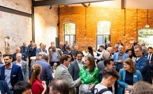 Viele Menschen in Business-Kleidung unterhalten sich in einem Raum mit Backsteinwänden bei einer Networking-Veranstaltung.