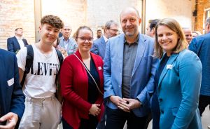 Vier Personen posieren lächelnd für ein Foto bei einer Veranstaltung in einem Backsteingebäude.