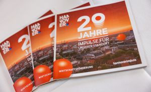 Drei orangefarbene Broschüren mit Aufschrift „20 Jahre Impulse für unseren Standort – Hannover Wirtschaftsförderung".