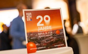 Aufsteller mit Text „20 Jahre – Impulse für unseren Standort", Hannover-Logo, Stadtpanorama, auf einem Tisch.