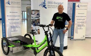 Mann steht neben grünem Elektro-Lastenrad vor BBS Burgdorf Berufsbildende Schulen Ausstellungsstand.