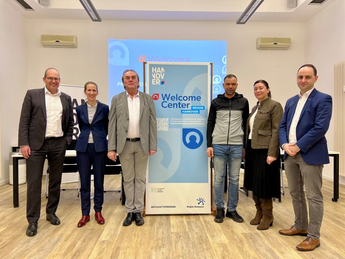 Sechs Personen stehen vor einem Rollup-Banner des Welcome Centers Region Hannover in einem hellen Veranstaltungsraum.
