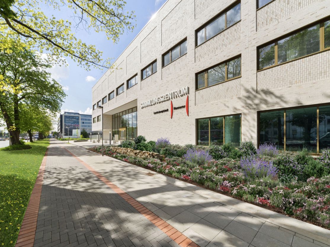 Modernes weißes Bürogebäude mit Aufschrift „Verwaltungszentrum", bepflanztem Vorgarten und gepflastertem Gehweg, Hannover.