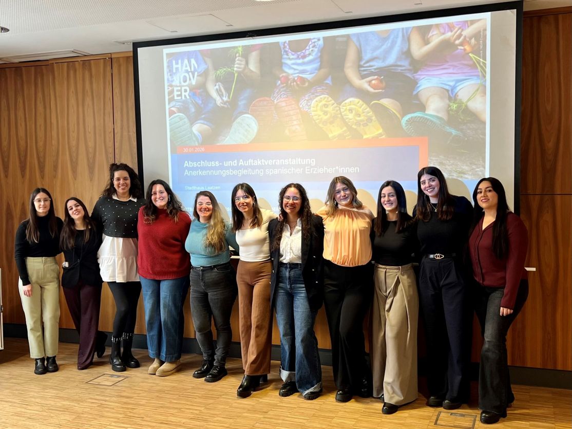 Gruppe von elf Frauen steht lächelnd vor einer Präsentationsleinwand mit deutschem Text in einem Konferenzraum.