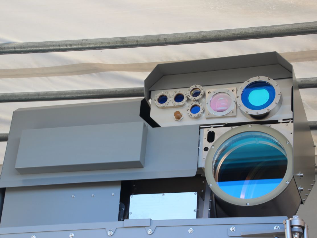 Graues militärisches Gerät mit mehreren optischen Linsen und Sensoren, montiert unter einem Vordach.