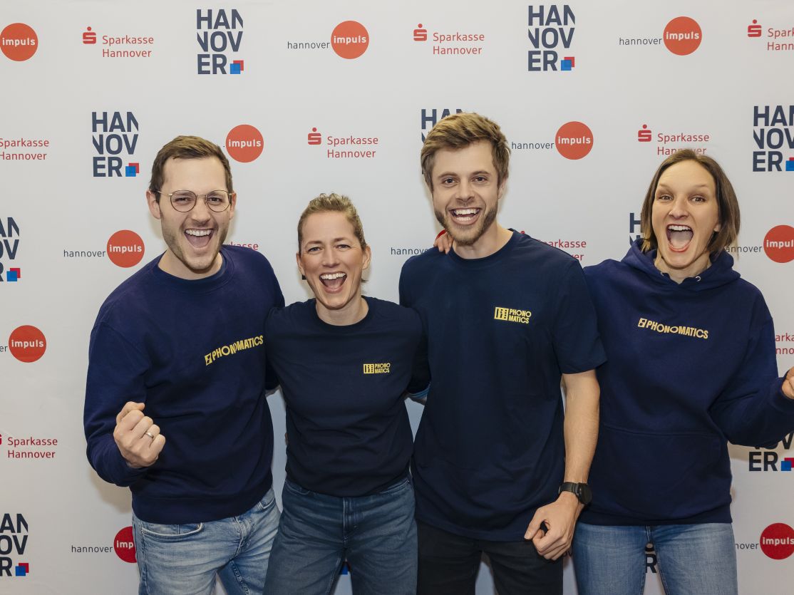 Vier Personen in dunkelblauen Sweatshirts posieren lächelnd vor einem Sparkasse-Hannover-Banner.
