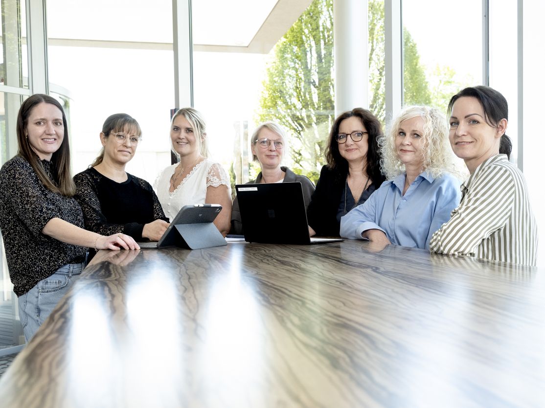 Sieben Frauen stehen nebeneinander und lächeln in die Kamera