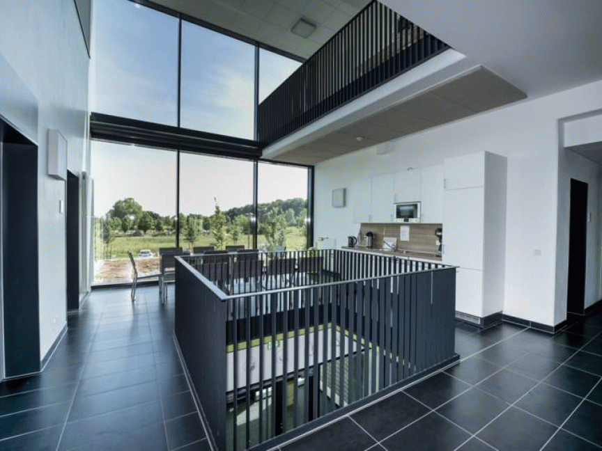 Moderner Innenraum mit dunklem Treppengeländer, Glasfassade, Blick auf Grünfläche und weißer Küche im Hintergrund.