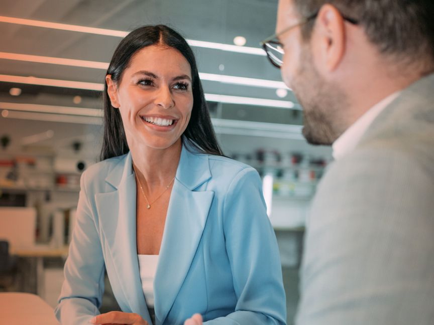 „Zwei Personen in Businesskleidung sitzen sich gegenüber und sprechen miteinander in einem Büro."