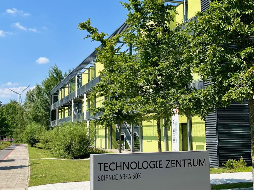 Schild „Technologie Zentrum Hannover, Science Area 30X" vor modernem Gebäude mit gelben Fassadenelementen und Bäumen.
