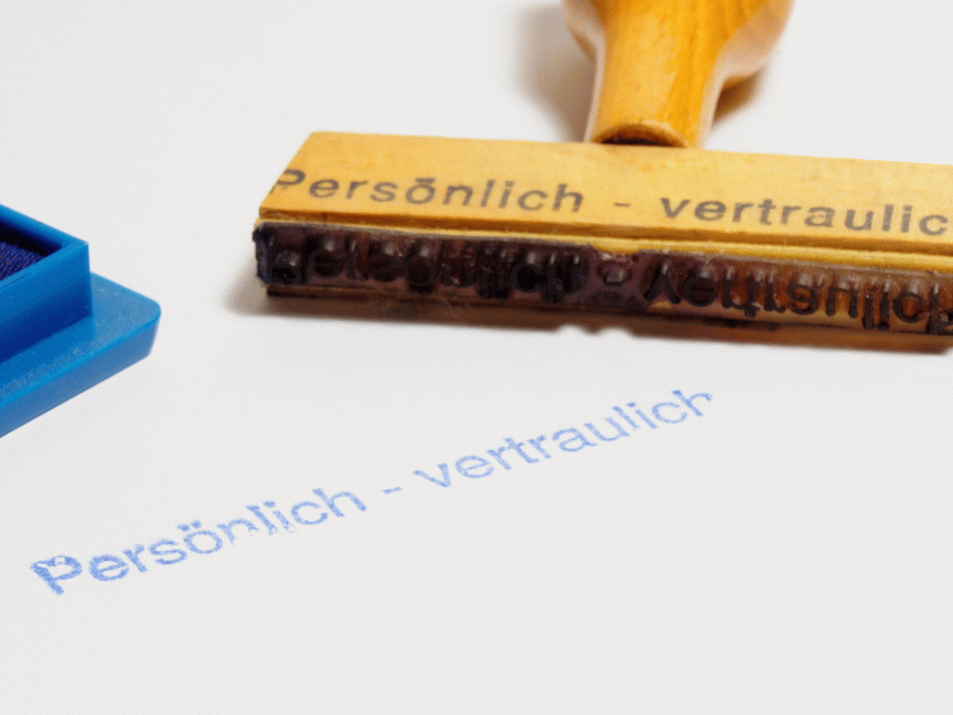 Holzstempel mit Aufdruck „Persönlich – vertraulich", daneben blaues Stempelkissen und Abdruck auf weißem Papier.