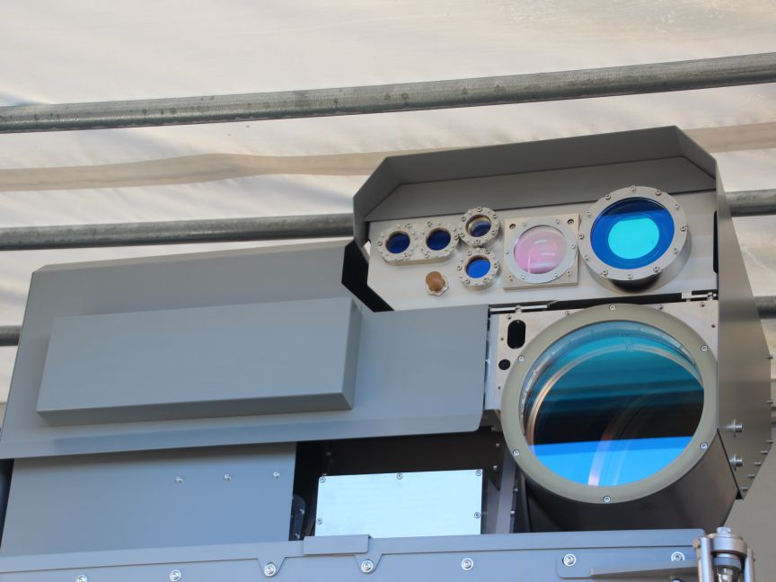 Graues militärisches Gerät mit mehreren optischen Linsen und Sensoren, montiert unter einem Vordach.