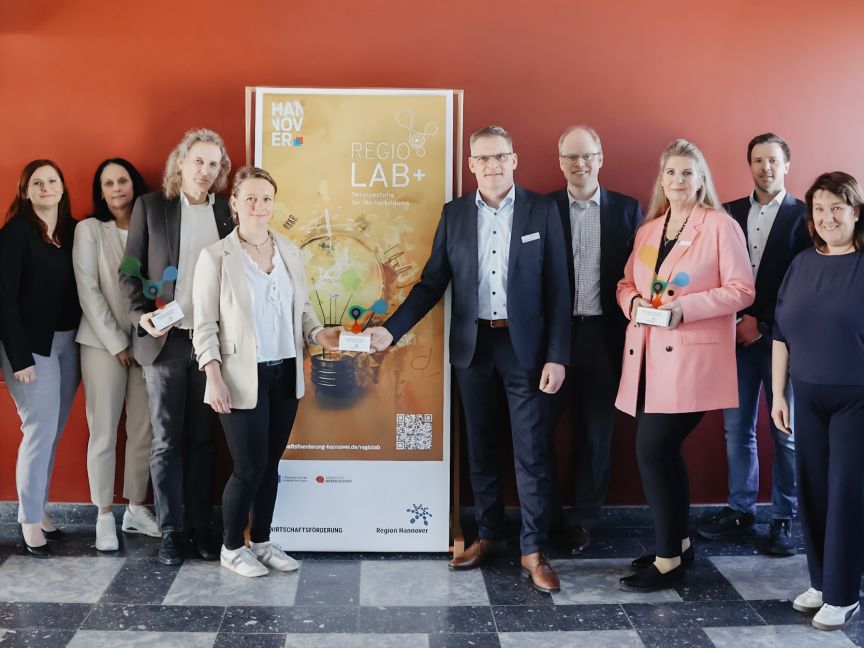 Gruppe von ca. 11 Personen steht vor einem Banner mit Aufschrift „REGIO LAB+" in einem Gebäude.