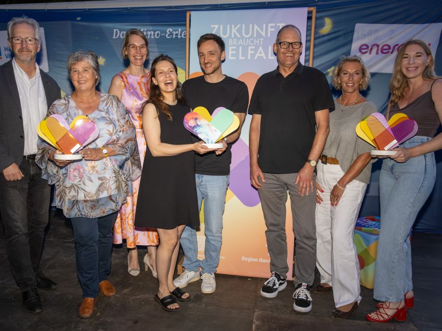 Mehrere Personen freuen sich und halten insgesamt drei Awards in der Hand.