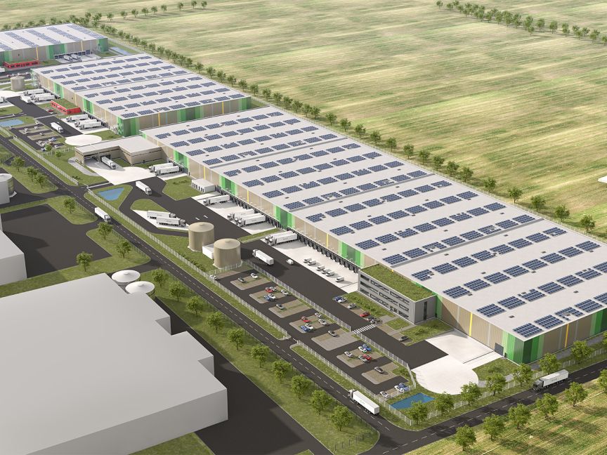 Luftaufnahme eines großen weißen Industriegebäudes mit Solarpanelen auf dem Dach, Parkplatz und umliegenden Feldern.