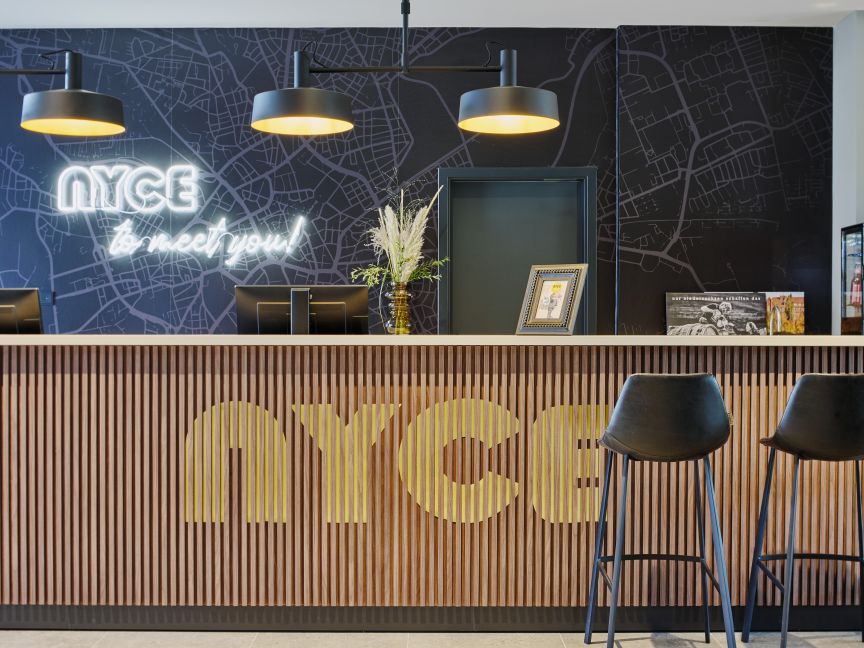 Hotelrezeption mit Holzverkleidung, „NYCE"-Logo, Neonschrift, zwei schwarzen Barhockern und Stadtkartenillustration.