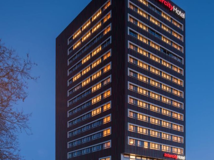 Modernes IntercityHotel-Hochhaus mit beleuchteten Fenstern in der Abenddämmerung, umgeben von einem gepflasterten Platz.
