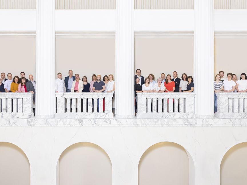 Gruppe von etwa 30 Personen steht auf einem weißen Marmor-Balkon eines klassizistischen Gebäudes.