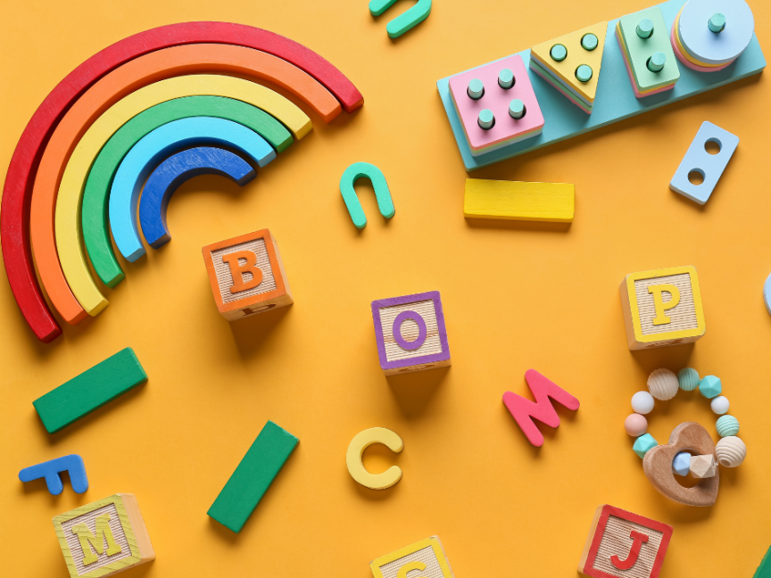 Bunte Holzspielzeuge auf orangem Hintergrund: Regenbogen, Buchstabenblöcke (B, O, P, M, C, S, J), Bausteine und Beißring.