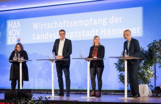 Vier Personen auf der Bühne an Stehtischen.