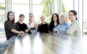 Sieben Frauen stehen nebeneinander und lächeln in die Kamera