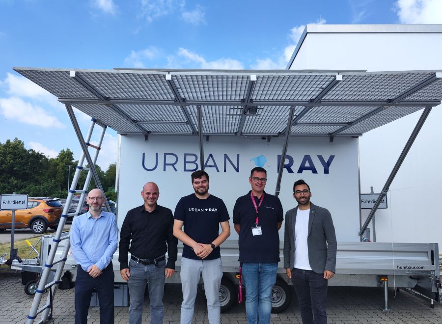Fünf Männer stehen vor einem weißen Anhänger mit Solarpanelen und dem Schriftzug „Urban Ray".