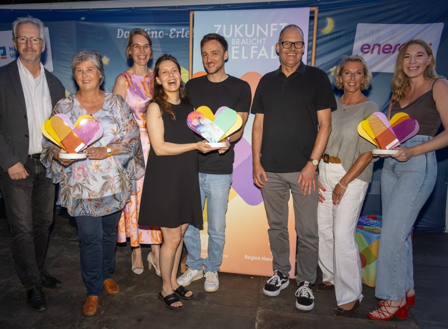 Mehrere Personen freuen sich und halten insgesamt drei Awards in der Hand.