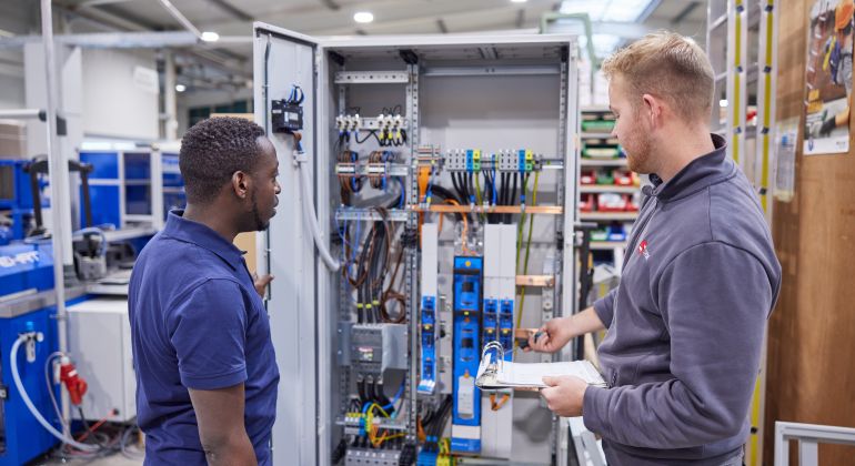 Zwei Männer in der Werkstatt bei der Arbeit vor einem Kabelschrank.