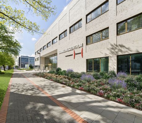 Modernes weißes Bürogebäude mit Aufschrift „Sammlungszentrum", bepflanztem Vorgarten und gepflastertem Gehweg, Hannover.