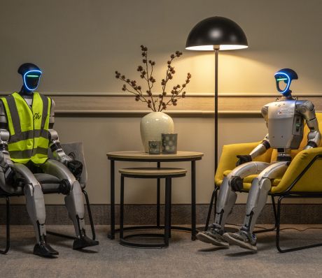 Zwei Roboter sitzen auf Stühlen an einem Tisch.