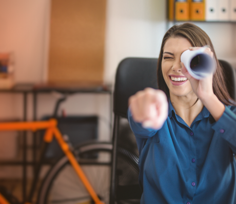 Frau guckt durch zusammengerolltes Papier wie ein Fernglas.
