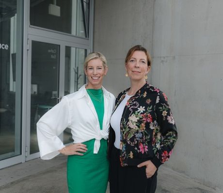 Zwei Frauen stehen vor einem Gebäude mit der Aufschrift „Idea Space". Eine trägt Grün-Weiß, die andere ein Blumenoberteil.