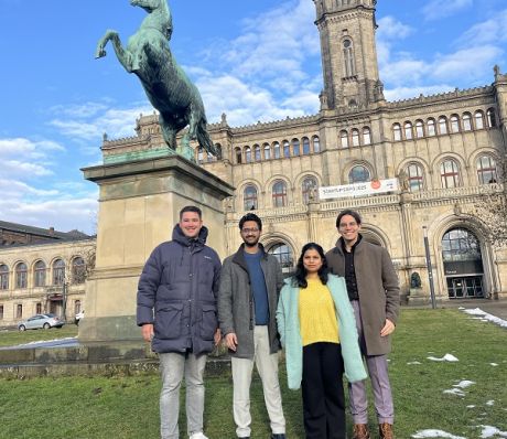 Vier Personen stehen vor einem historischen Gebäude mit einer grünen Pferdestatue. Winter, teilweise Schnee.