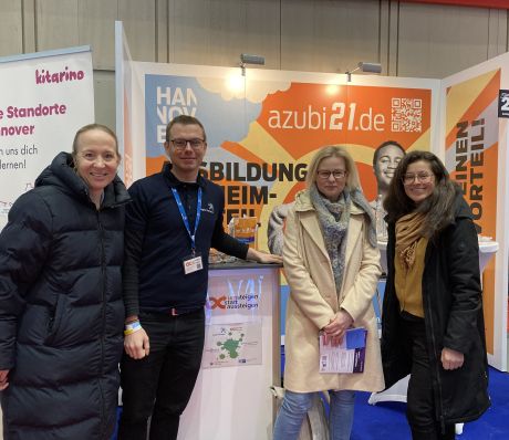 Vier Personen stehen an einem Messestand mit Bannern von „azubi21.de" und „Kitarino" in einer Ausstellungshalle.