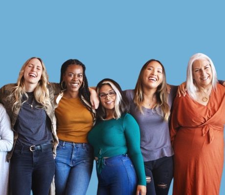 Fünf lachende Frauen verschiedener Ethnien und Altersgruppen stehen eng beieinander vor blauem Hintergrund.