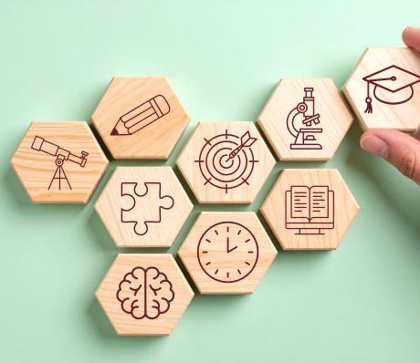 Holzbausteine mit verschiedenen Symbolen wie Uhr, Stift, Fernrohr, Puzzlestein, Buch, Gehirn.